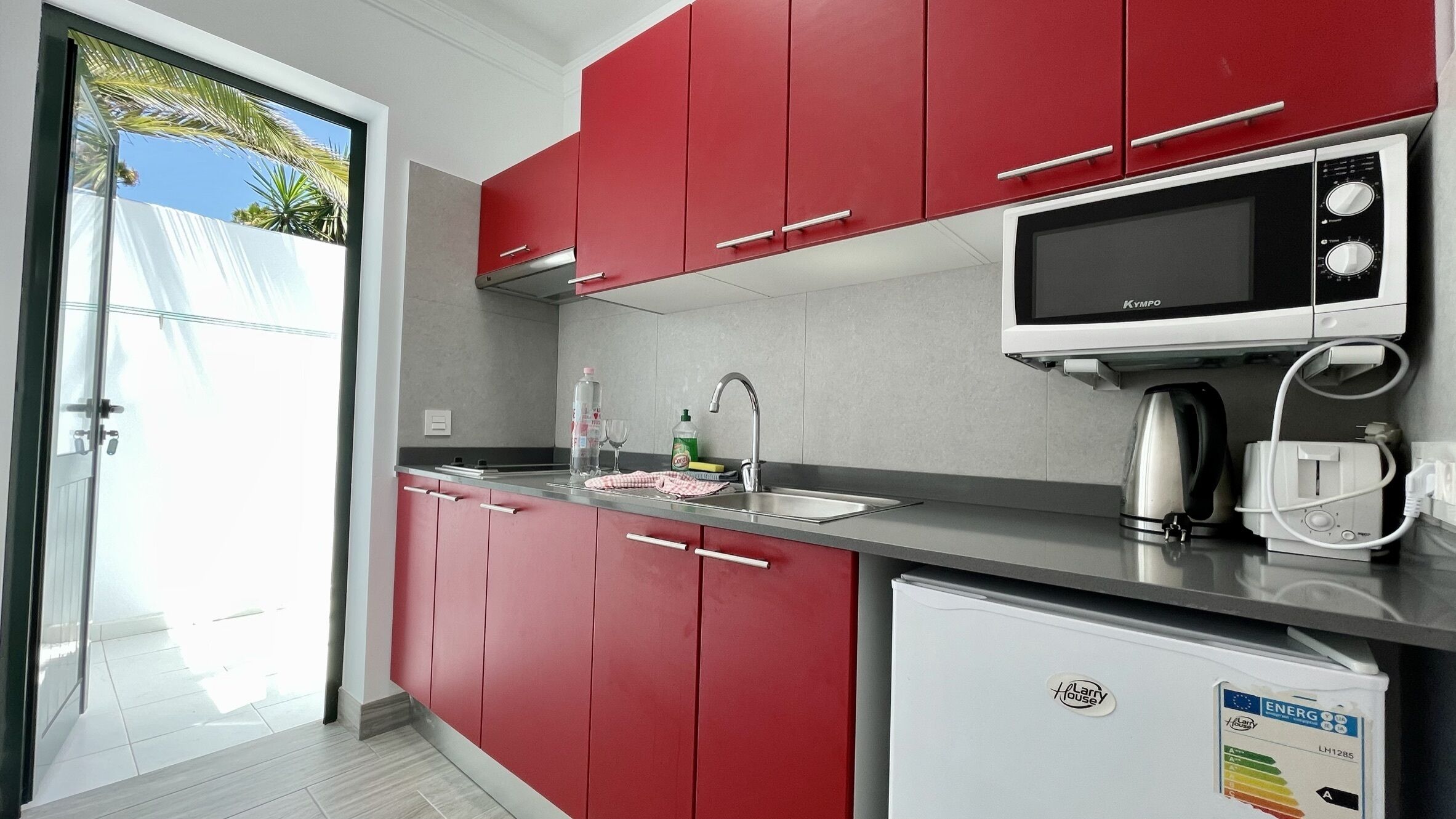 Una cocina moderna con armarios rojos, un microondas integrado y un refrigerador pequeño.