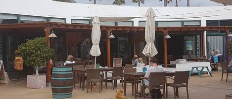 An outdoor cafe area with tables and chairs, umbrellas, and a dog lying on the ground.