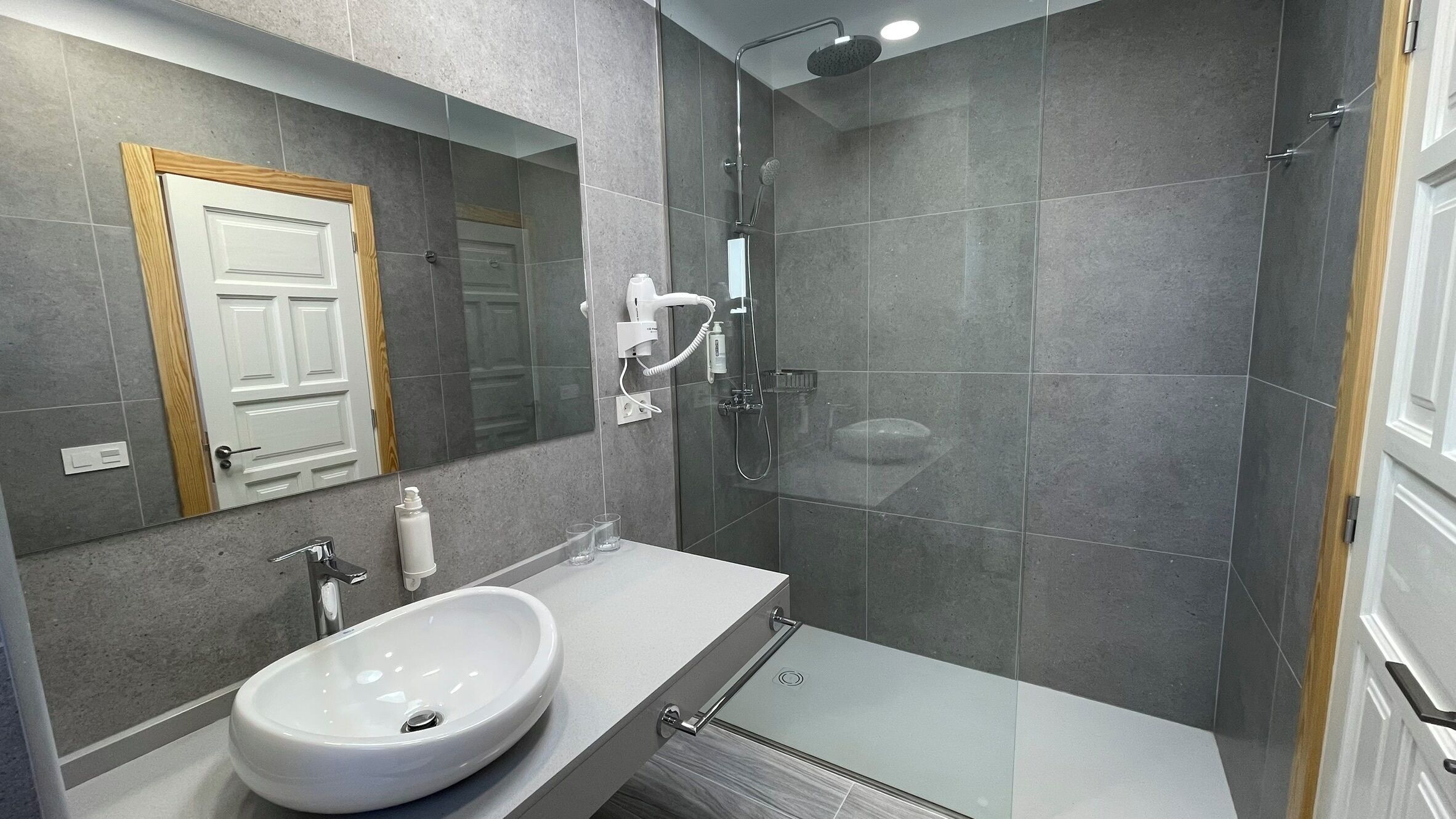 A modern bathroom with a large mirror, a white sink, and a glass-enclosed shower area.