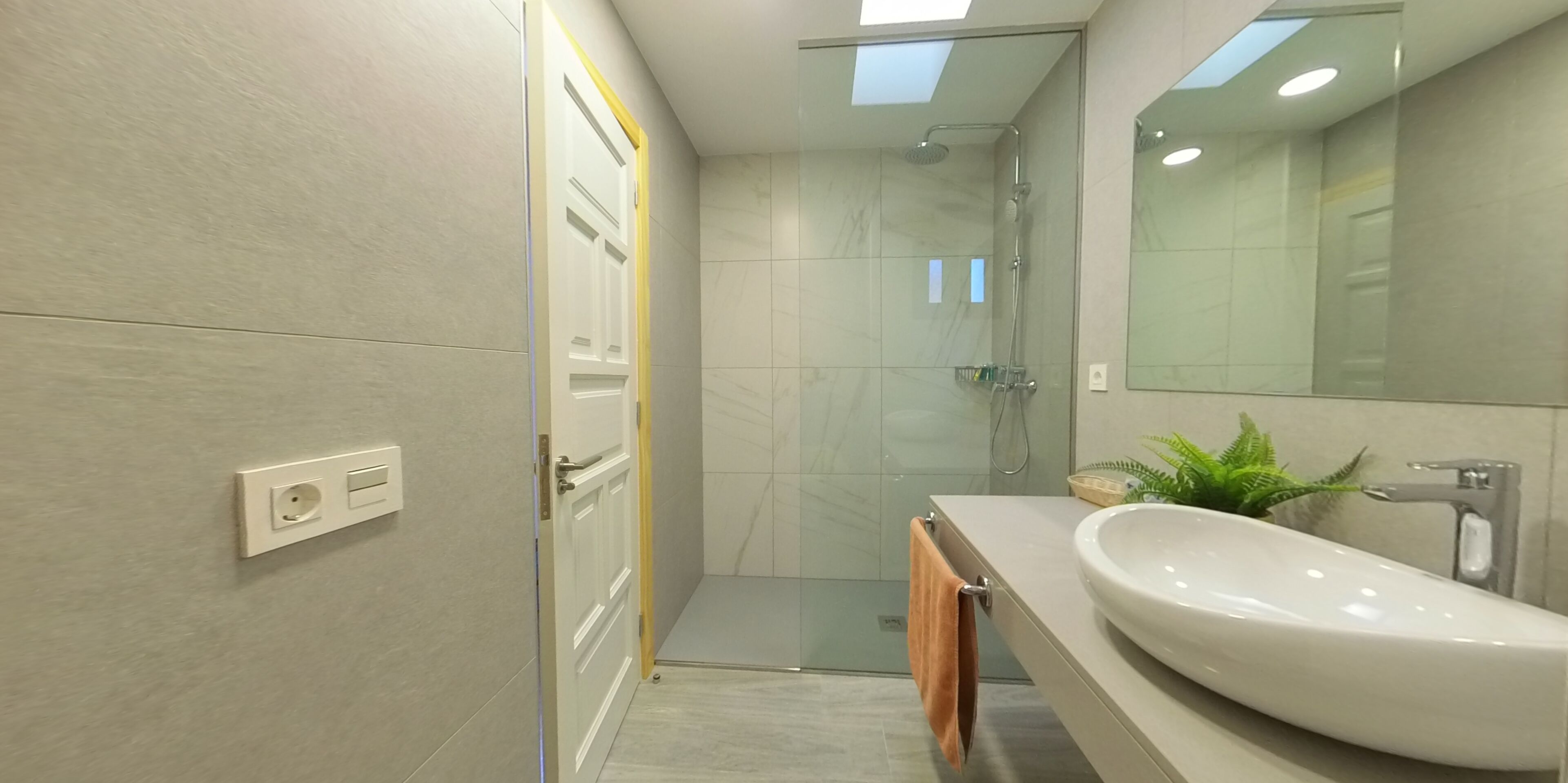 Un baño moderno con cabina de ducha de vidrio, un espejo grande y un lavamanos blanco.