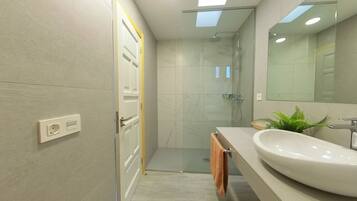 Un baño moderno con cabina de ducha de vidrio, un espejo grande y un lavamanos blanco.