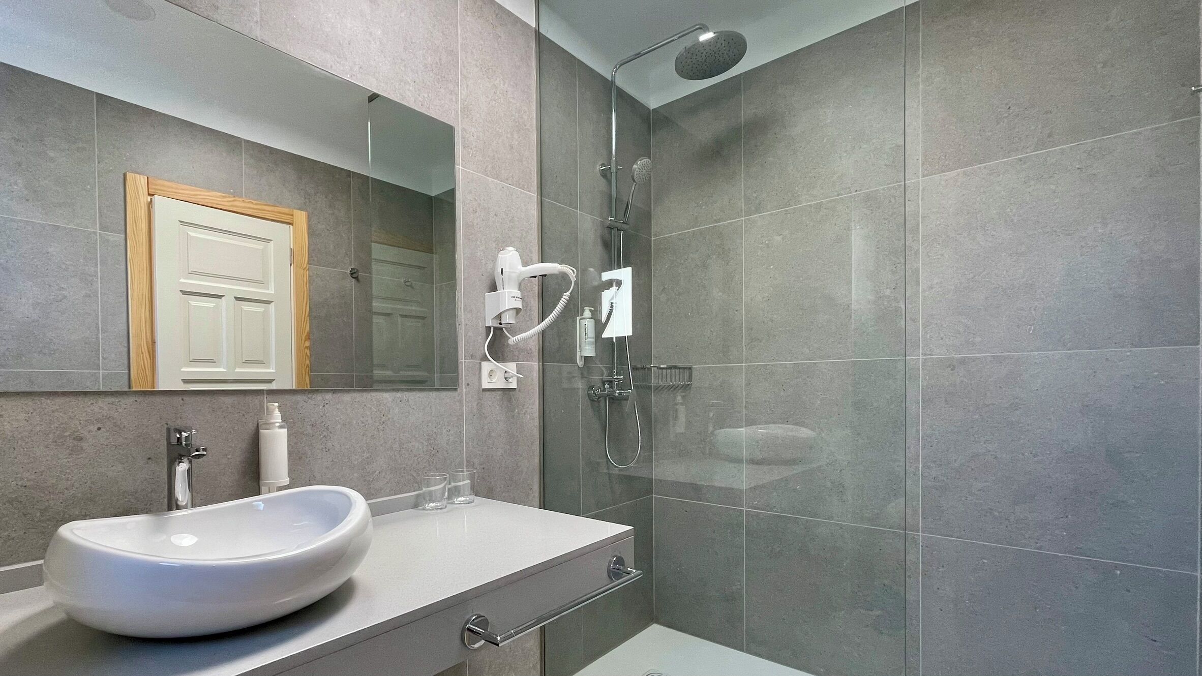 Un baño moderno con cabina de ducha de vidrio, un lavabo blanco y un espejo sobre él.