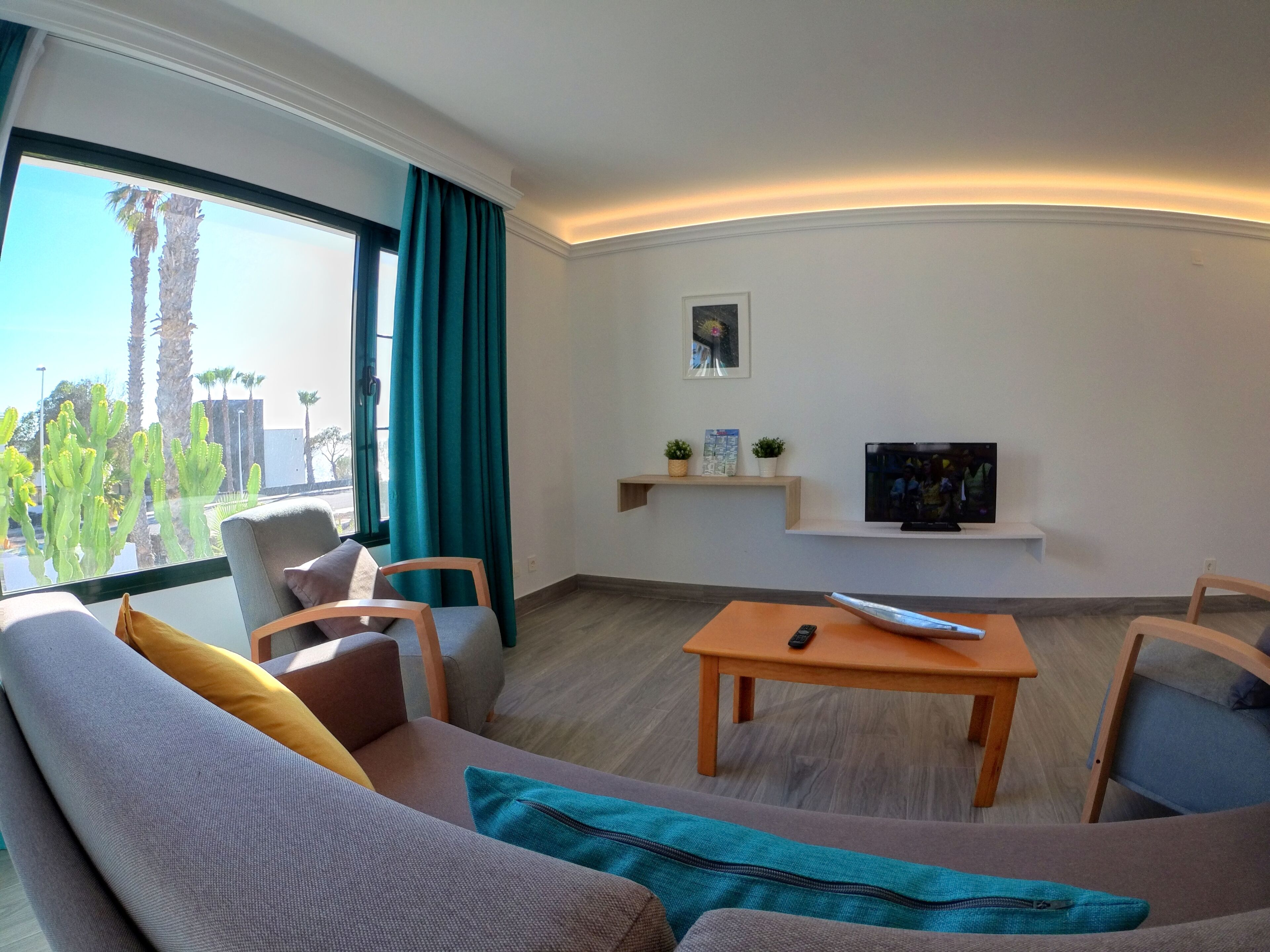 A modern living room with a sofa, chairs, a coffee table, a TV, and a window with curtains.