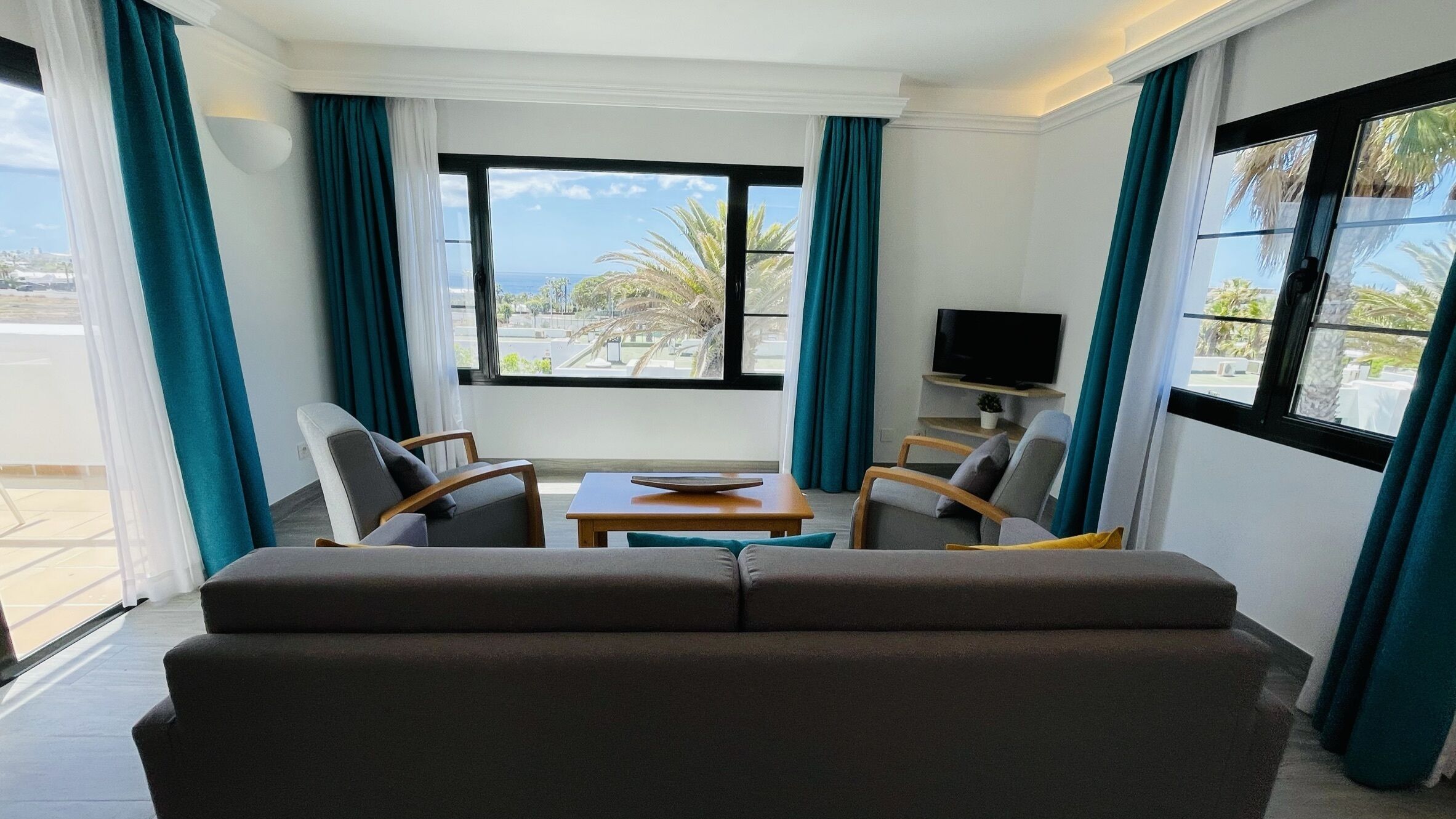 Una sala de estar moderna con un sofá, dos sillones, una mesa de centro y un televisor sobre un mueble bajo.