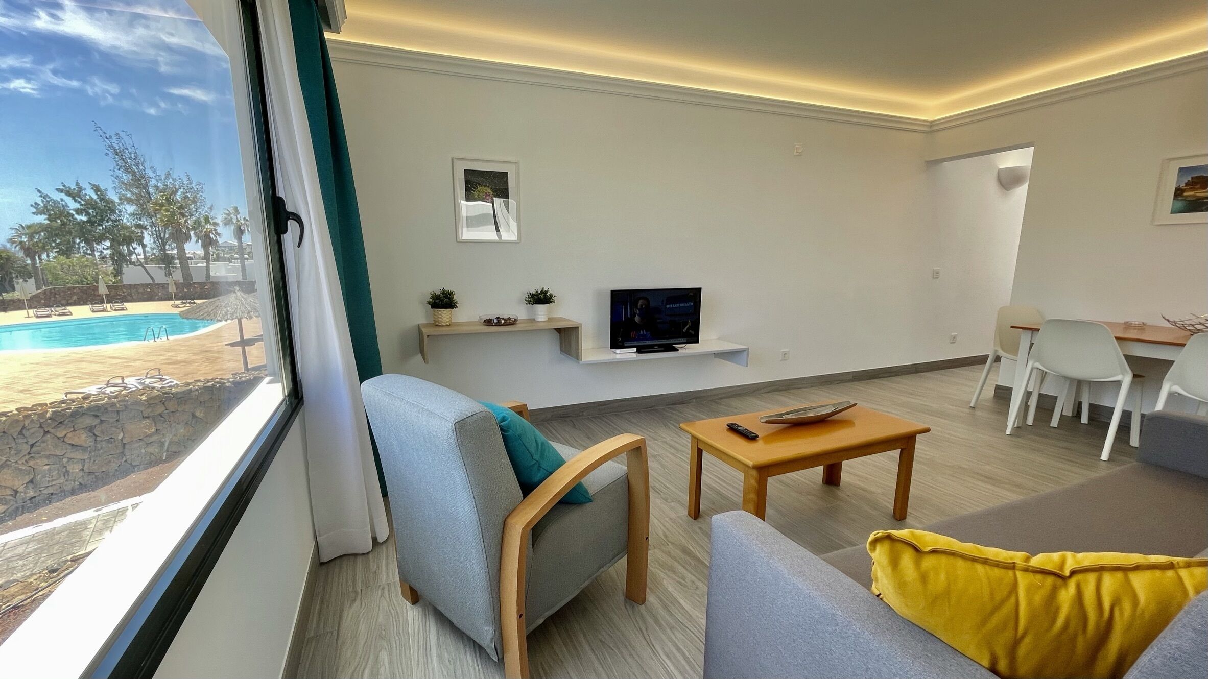 A modern living room with a sofa, a coffee table, a TV, and a view of a swimming pool outside.