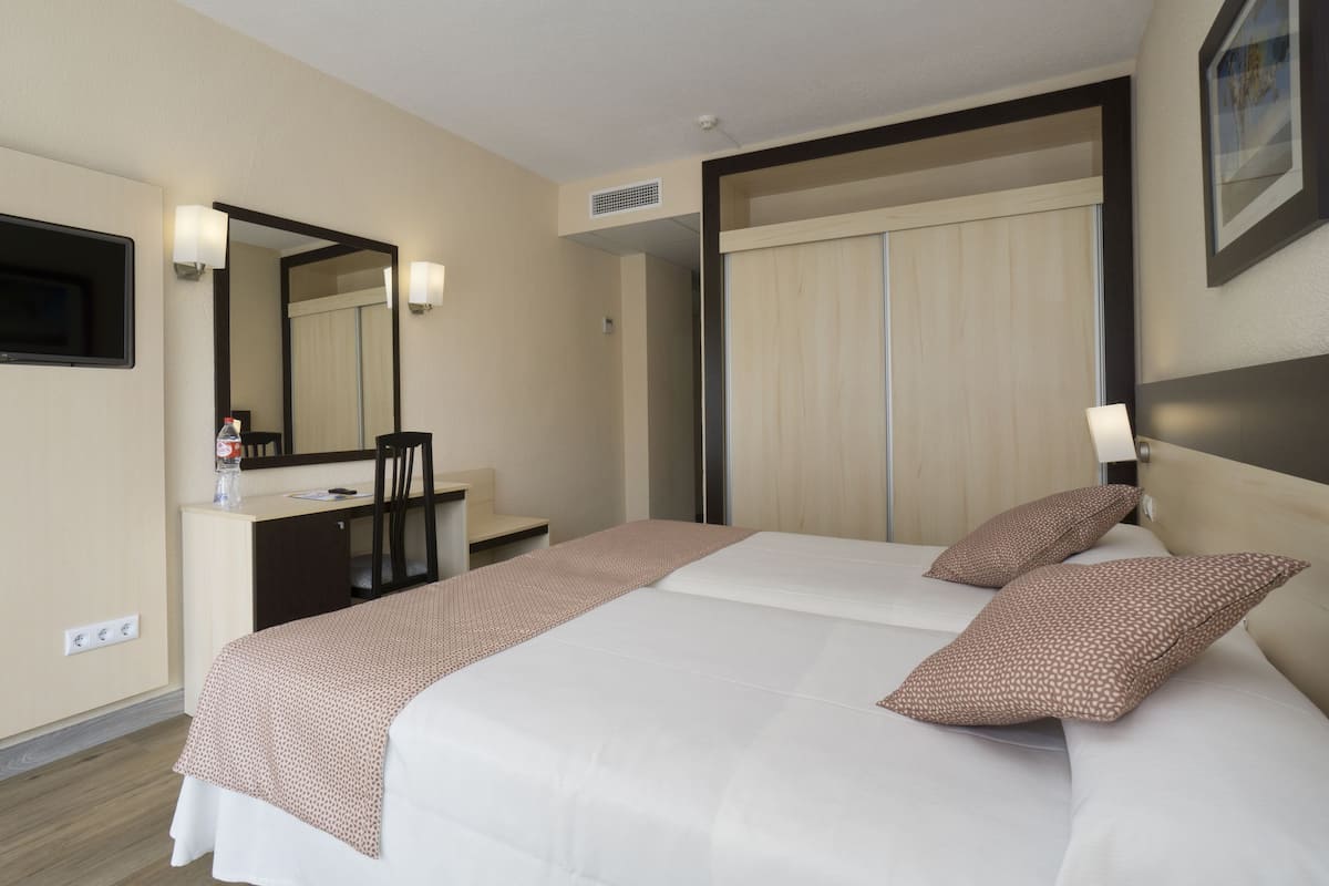 A hotel room with a bed, a desk, a chair, a mirror, and a wardrobe.