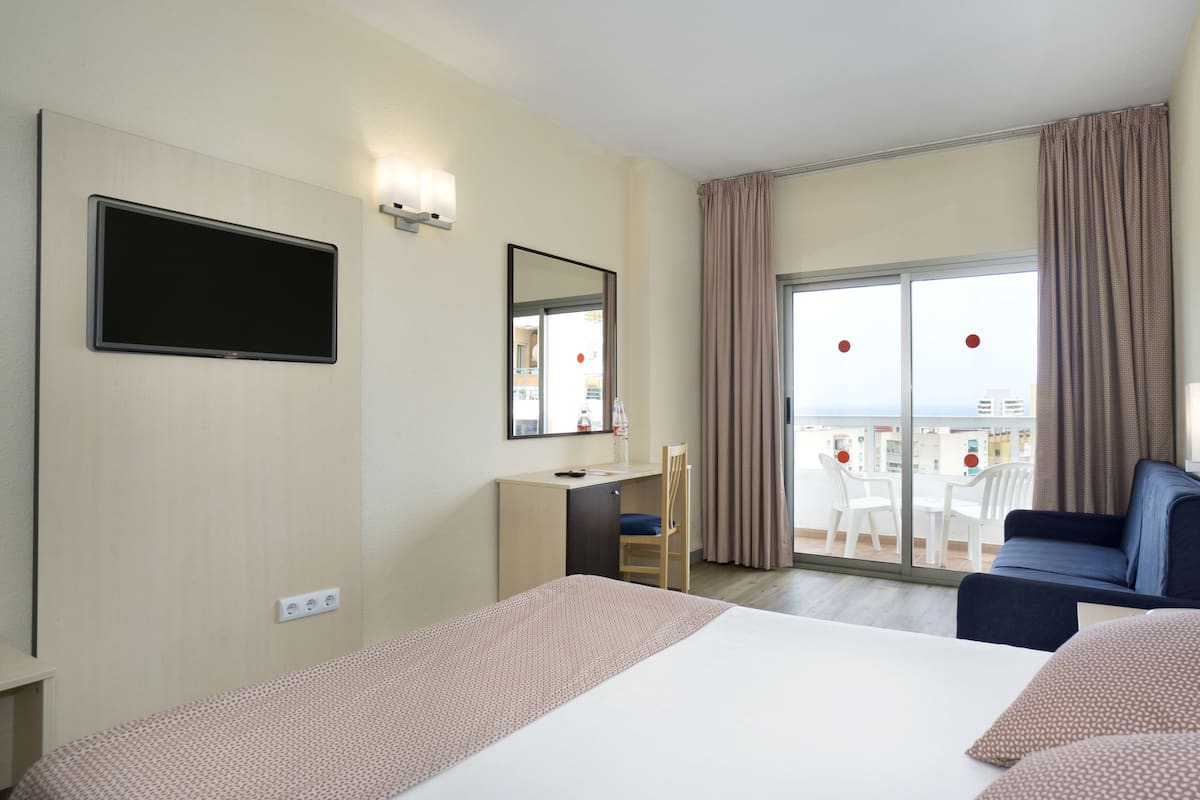 A hotel room with a bed, a desk, a chair, a TV, a balcony with a view, and curtains.