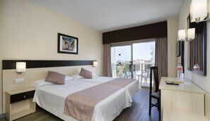 Une chambre d’hôtel avec un grand lit, un bureau, une chaise, un balcon donnant sur la ville et un tableau au mur.