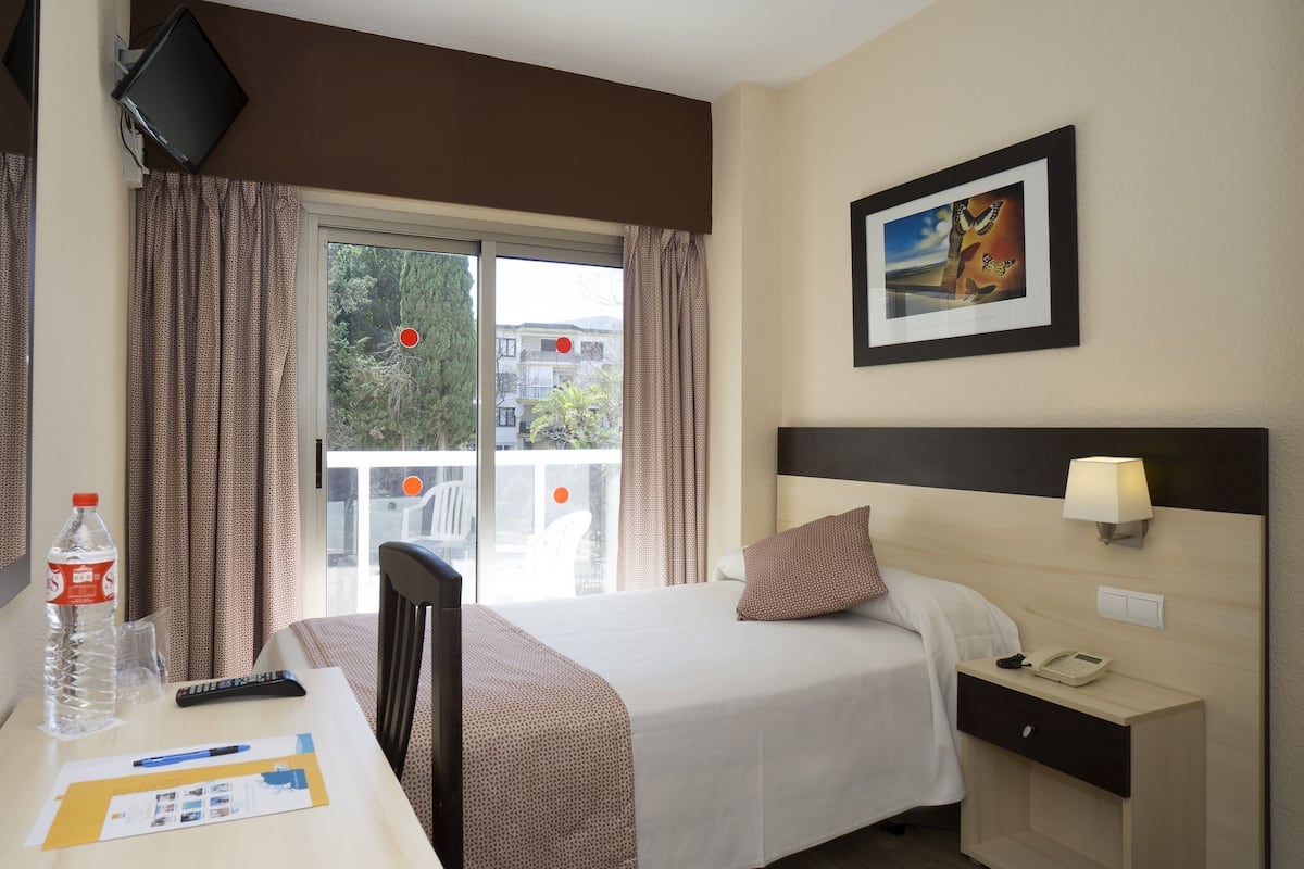 A hotel room with a bed, bedside table, lamp, and a painting on the wall.