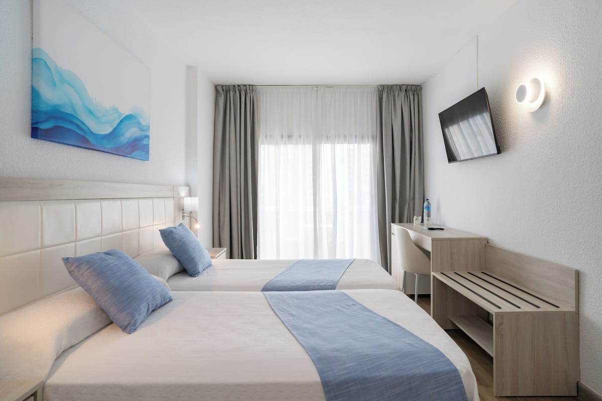 A hotel room with two beds, a desk, a chair, a TV, and a painting on the wall.