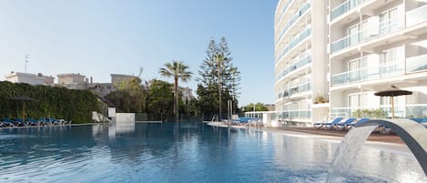 A swimming pool with lounge chairs and a water feature, surrounded by a modern building with balconies.
