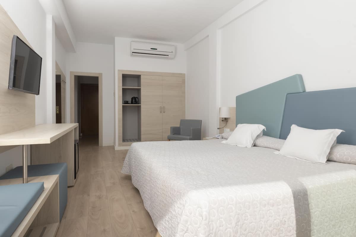 A hotel room with a bed, a desk, a chair, a wardrobe, and a TV mounted on the wall.