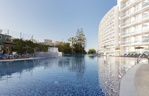 A swimming pool with blue mosaic tiles, surrounded by lounge chairs and a building with balconies. - Hotel Palia Las Palomas (Torremolinos)
