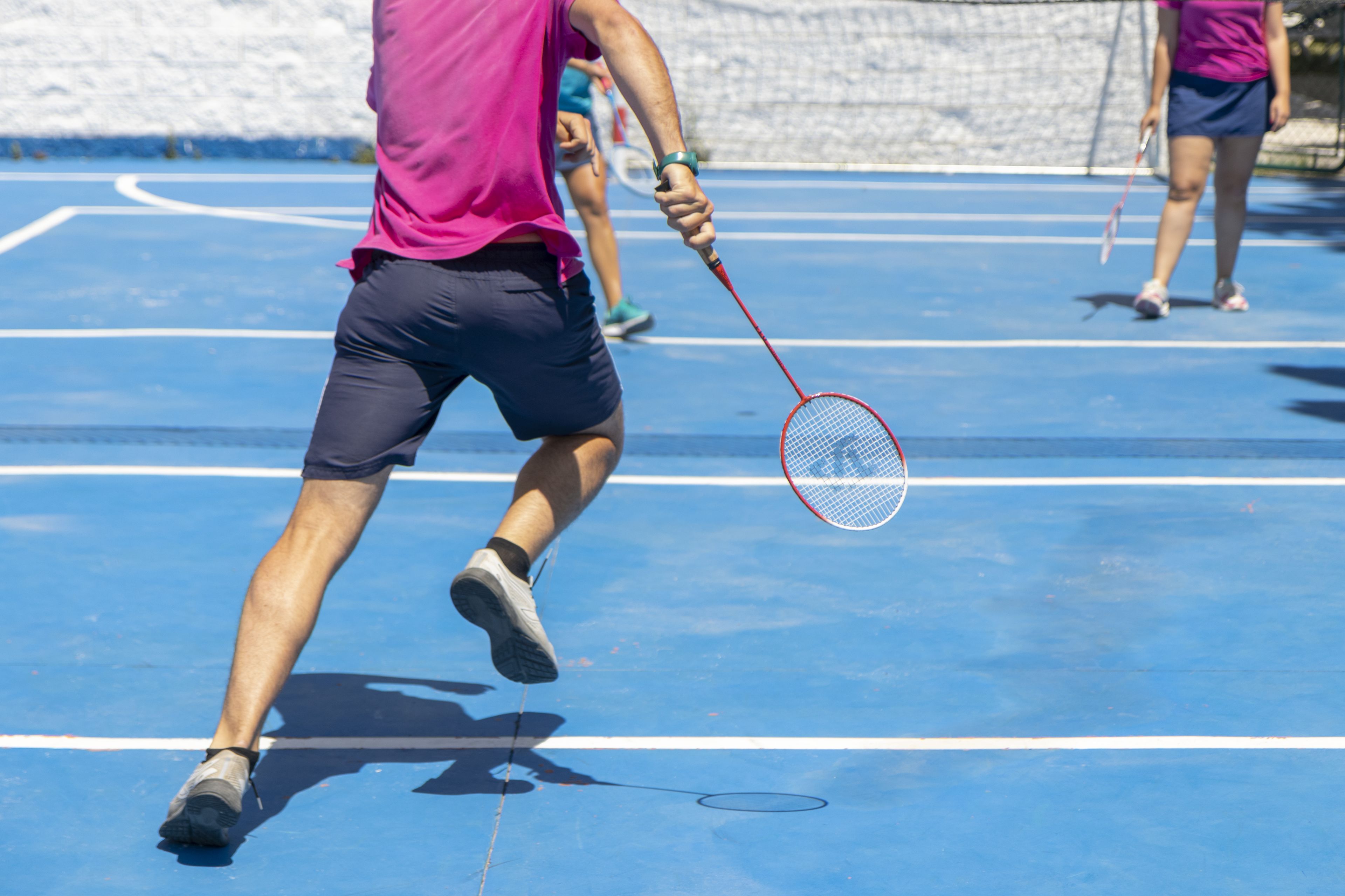 En tennisbane med net, linjer der afgrænser banen, og spillere i bevægelse.