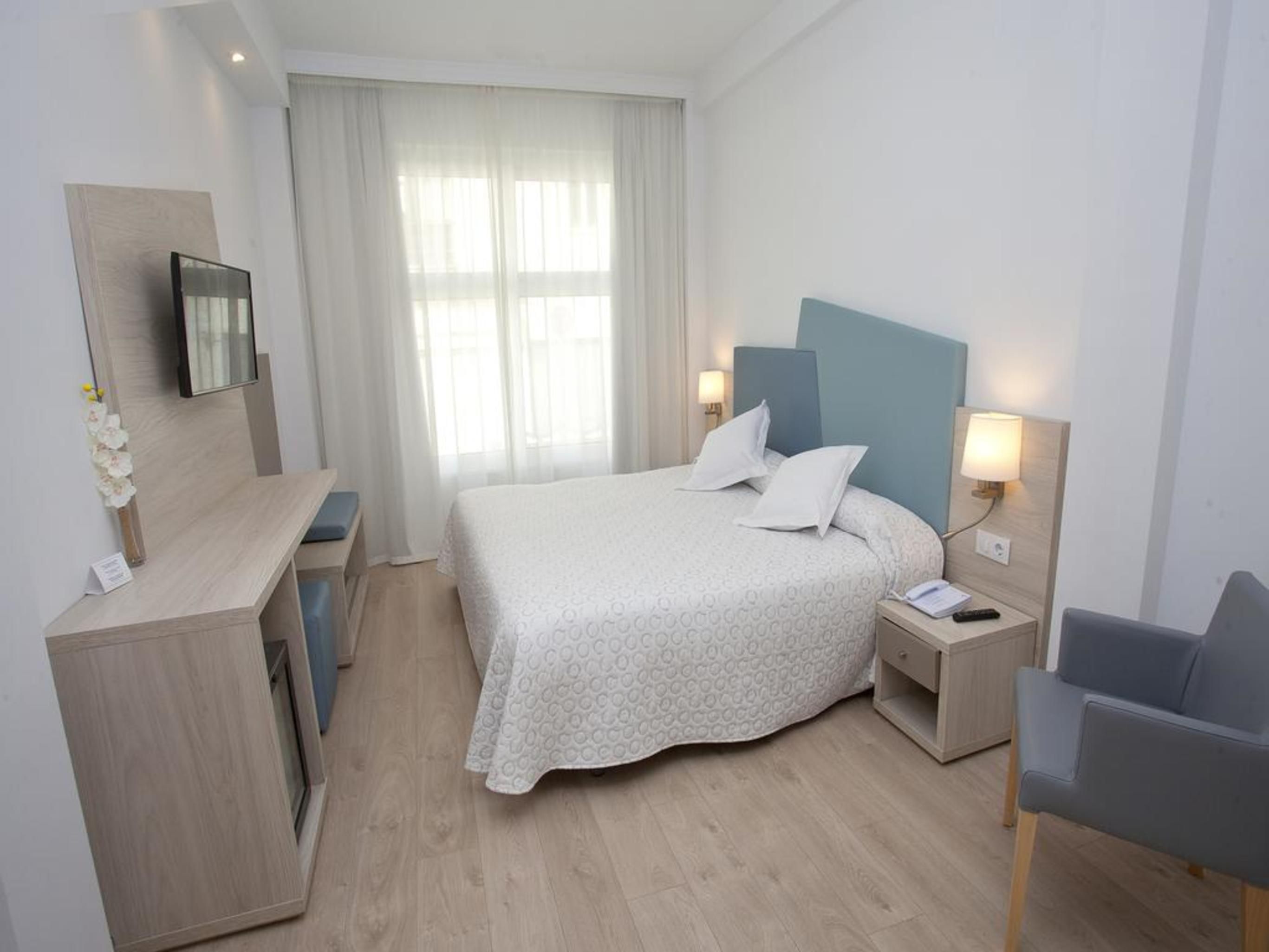 Habitación de hotel con cama, mesitas de noche, escritorio, silla y televisor montado en la pared.