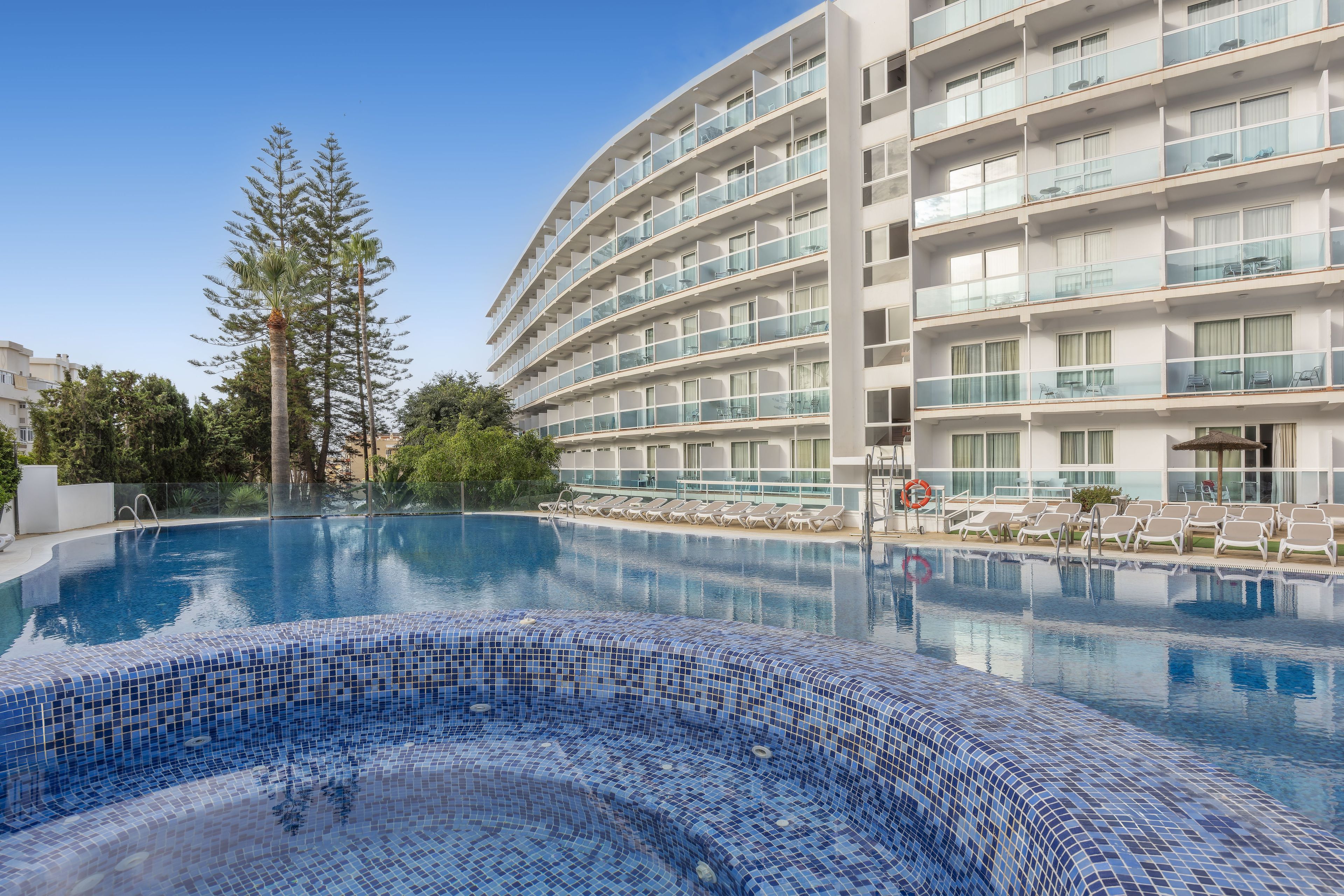 Un hotel con piscina, diversi balconi e cielo sereno.