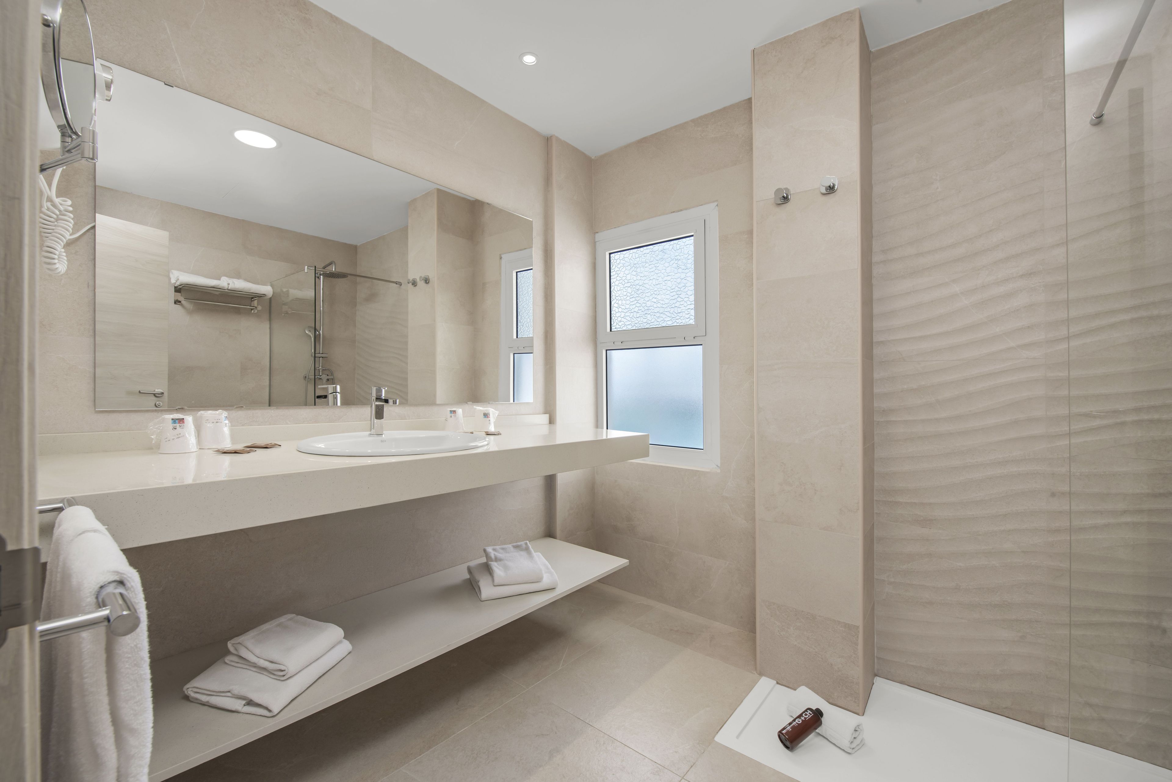 A modern bathroom with two sinks, a large mirror, and a shower area.