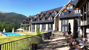 A hotel with multiple buildings featuring a modern architectural style, a pool, and outdoor seating areas. - Aparthotel Hg Cerler (Benasque)