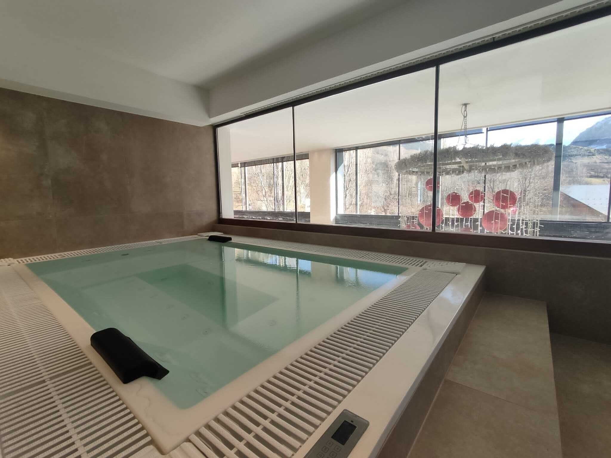 A large indoor swimming pool with a view of a snowy landscape through large windows.