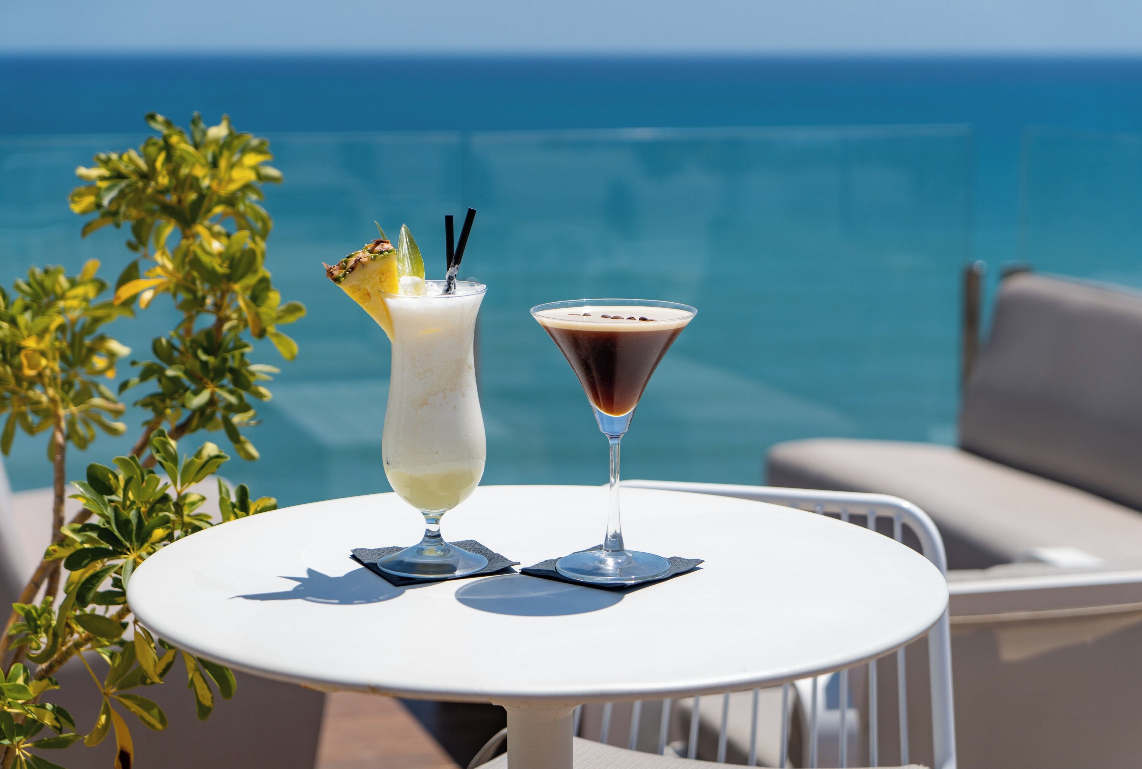 A table with two drinks and a view of the ocean.
