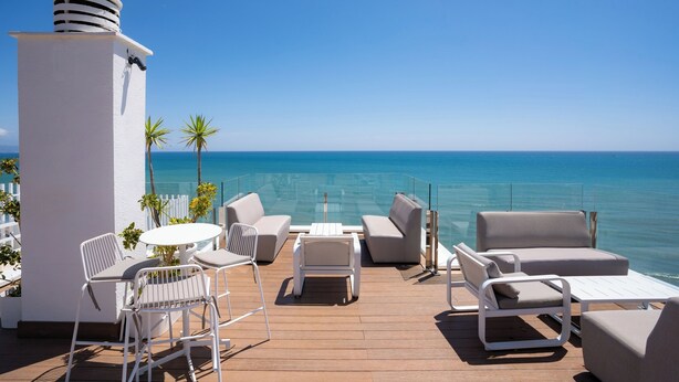 A deck with outdoor seating, a white column, and a view of the ocean. - Hotel La Barracuda (Torremolinos)