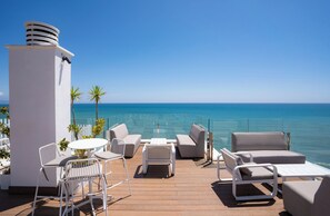 Een terras met buitenmeubels, een witte kolom en uitzicht op de oceaan.