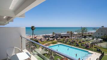 A pool area with a view of the sea, a beach, and a building with a sign that reads "LA MERIDINA".