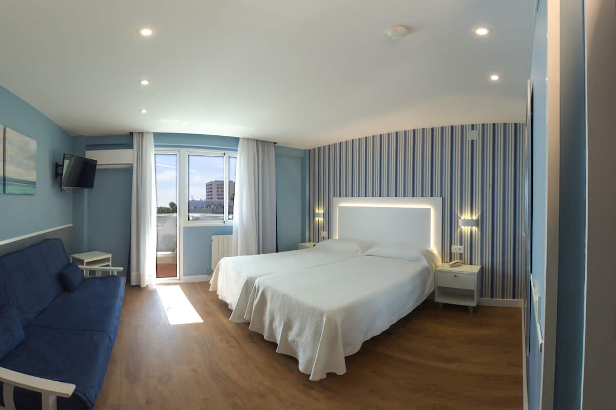 Habitación de hotel con dos camas, un sofá azul, televisión y vista a la ciudad.