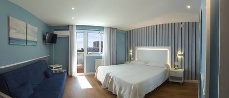 A hotel room with two beds, a blue sofa, a TV, and a view of the city.