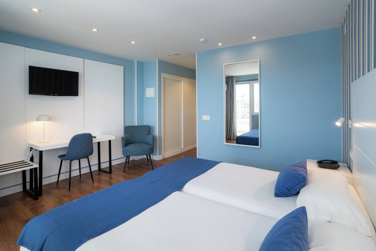 Una habitación de hotel con una cama, un escritorio, una silla, un televisor y un espejo.