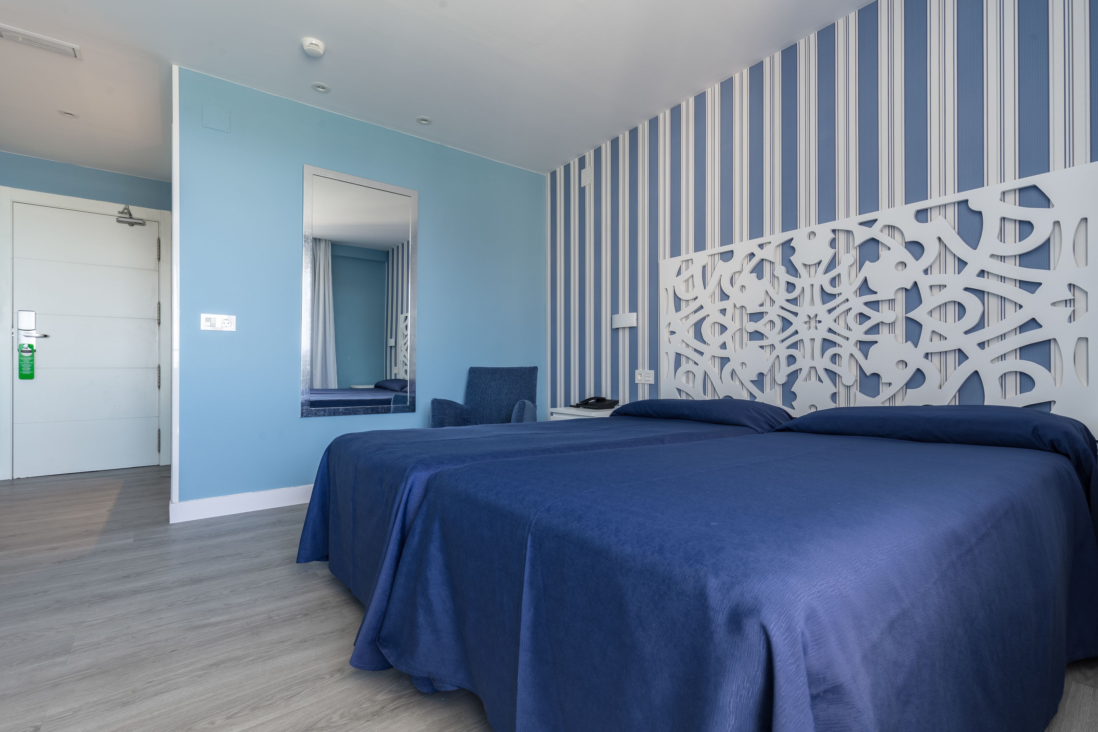 Een hotelkamer met een groot bed, een fauteuil, een bureau en een decoratief wandpaneel.