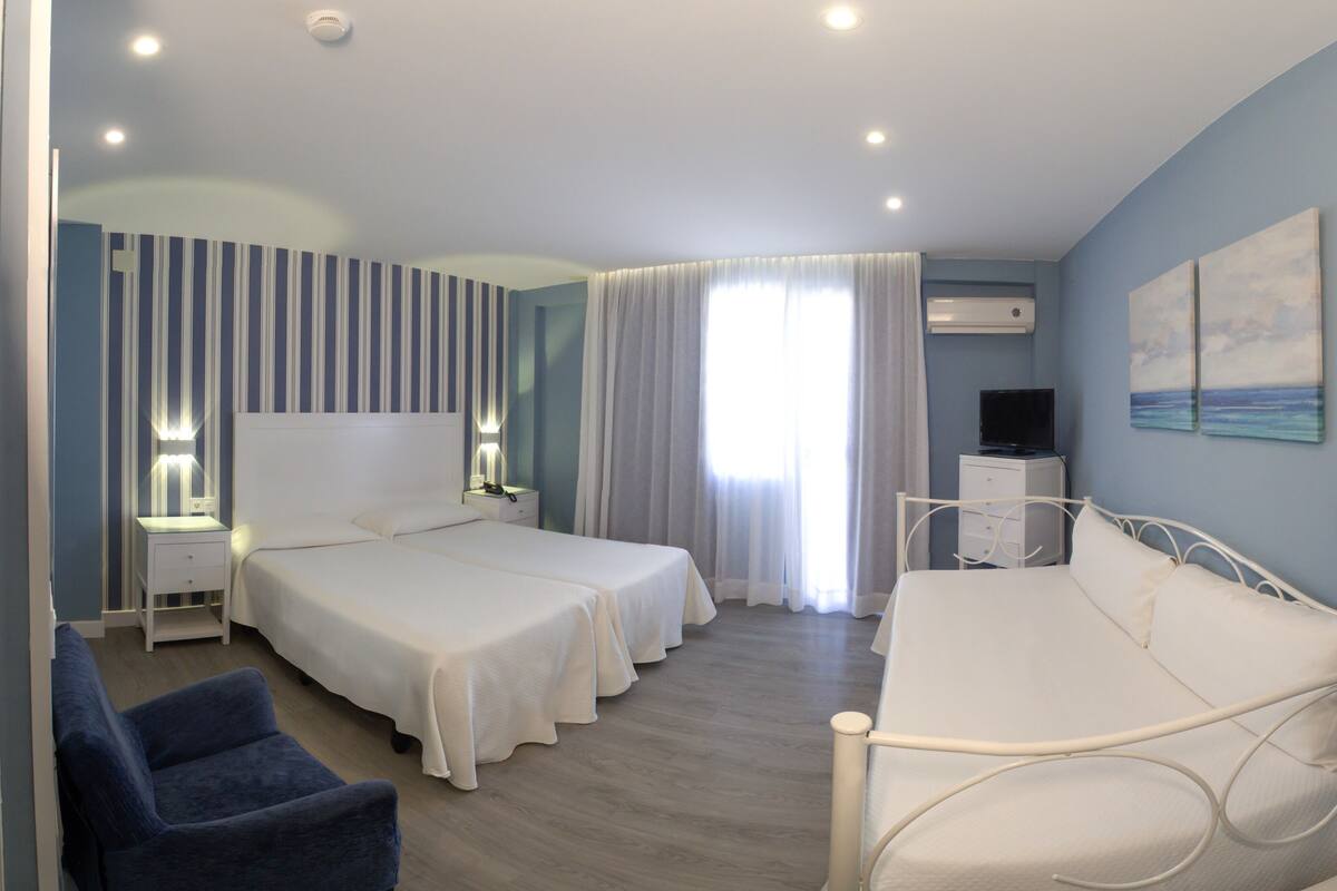 Habitación de hotel con dos camas, un escritorio, una silla, un televisor y un cuadro en la pared.