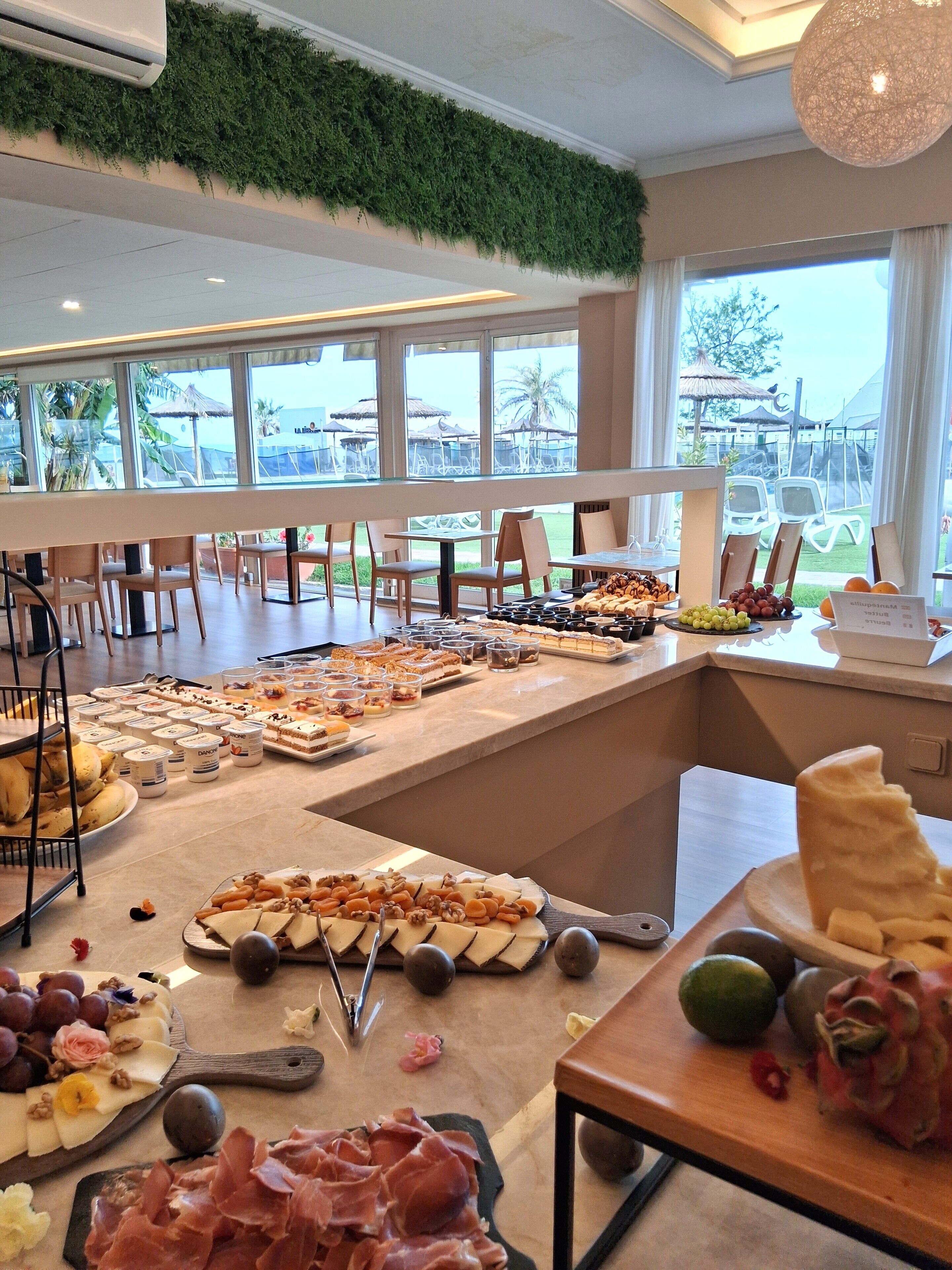 A buffet with various food items, a view of the outdoor area, and a ceiling with greenery.