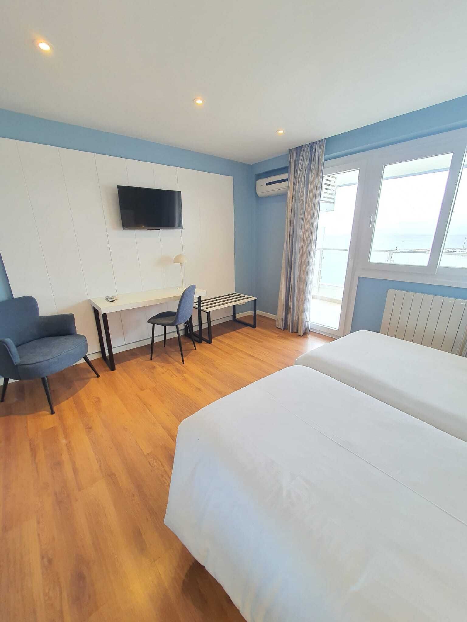 Une chambre d’hôtel comprenant un lit, un bureau avec une chaise, un téléviseur fixé au mur et une fenêtre avec des rideaux.