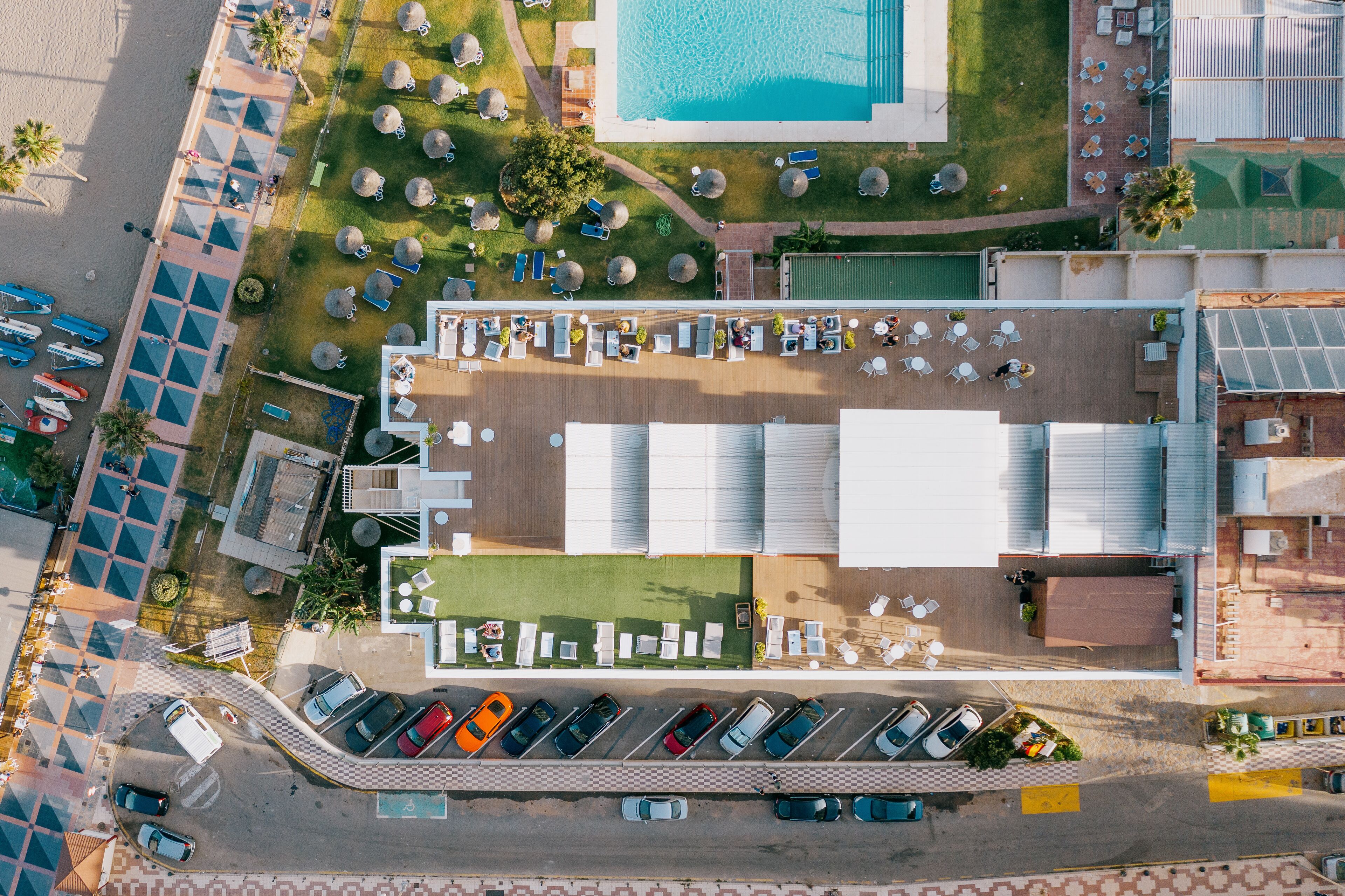 An aerial view of a hotel with a pool, multiple lounge areas, and a parking lot.