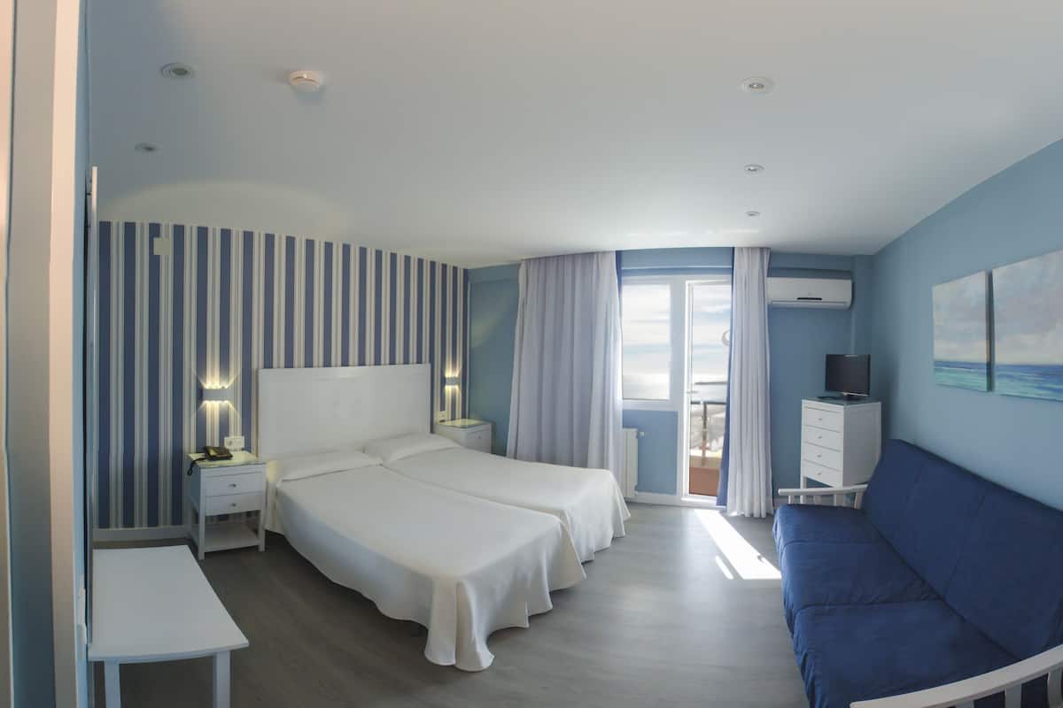 Habitación de hotel con una cama grande, un sofá, televisión y balcón con vistas.
