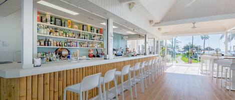 A bar area with a long counter, white chairs, and shelves stocked with bottles.