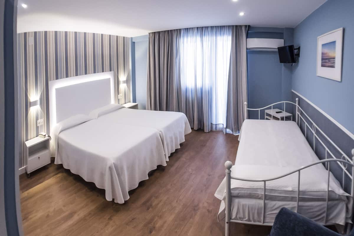Habitación de hotel con dos camas, televisión, una mesita y ventana con cortinas.