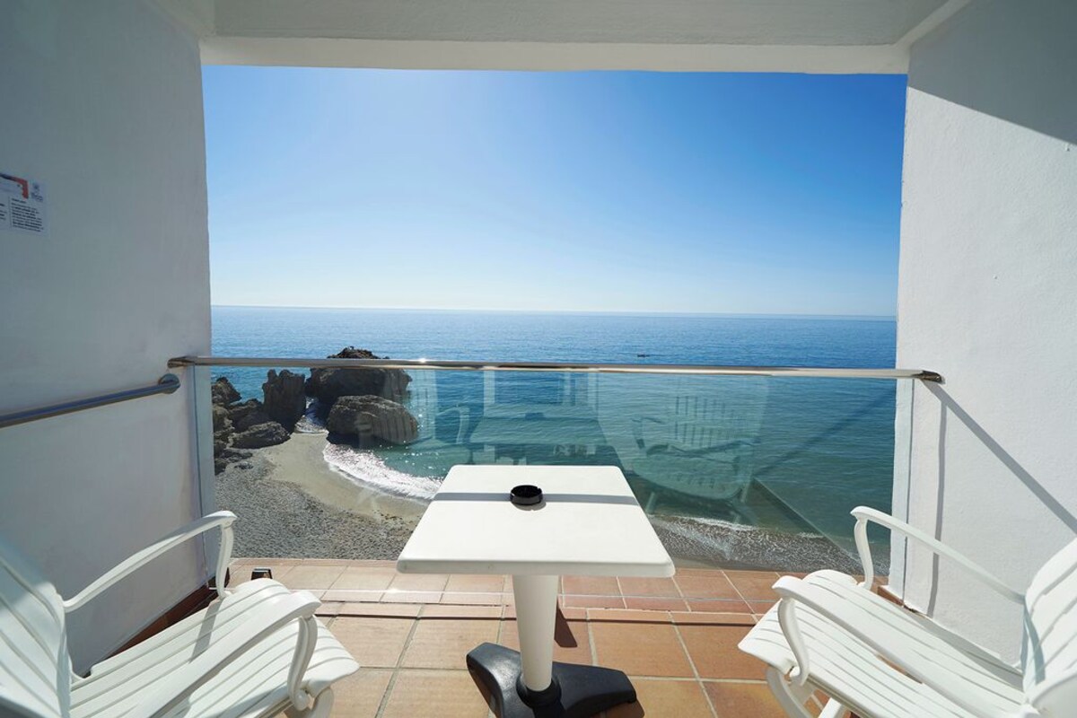 Un balcón con mesa y dos sillas, con vista a la playa y al mar.