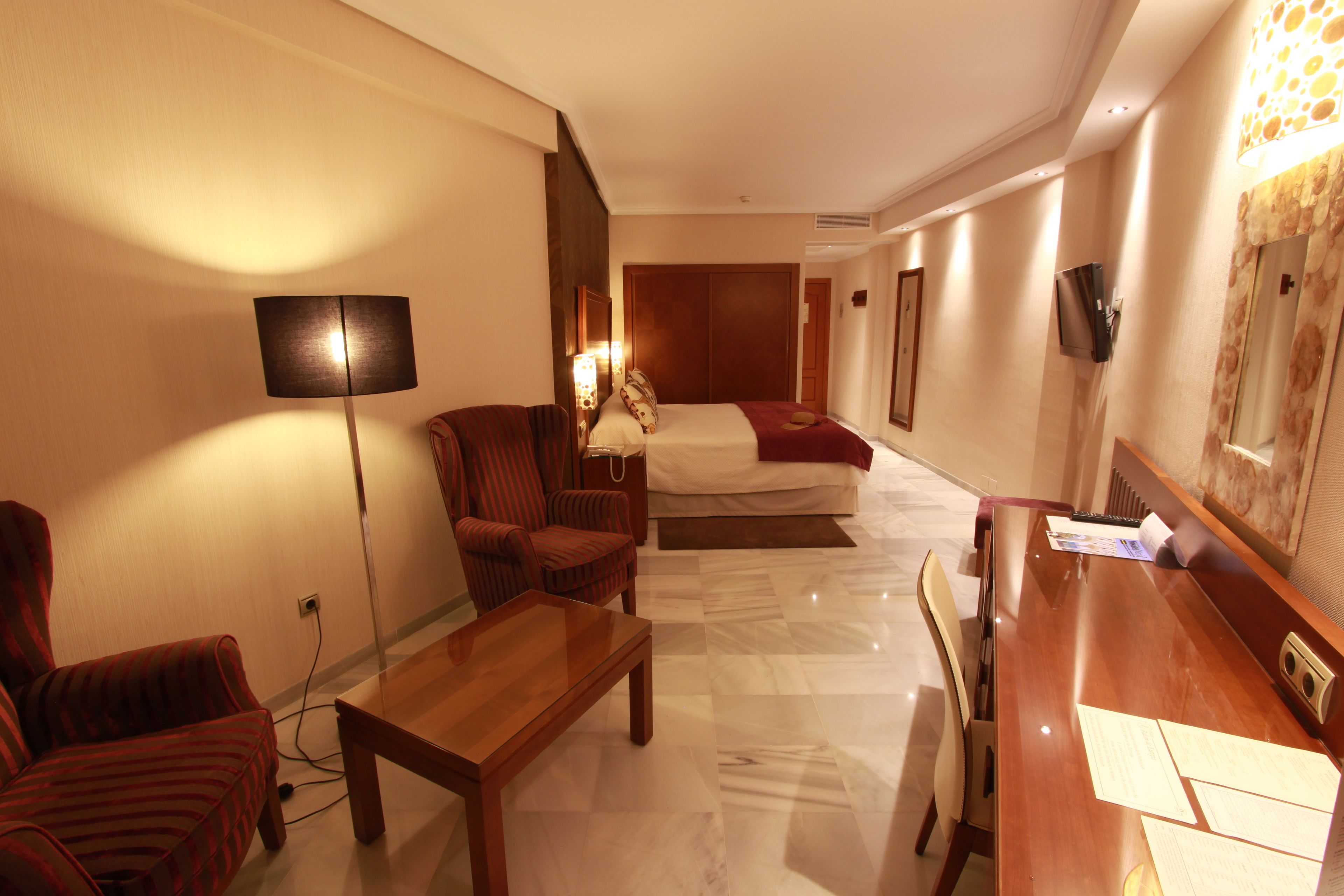Ein Hotelzimmer mit Bett, Schreibtisch, Stuhl, Lampe und Fernseher.