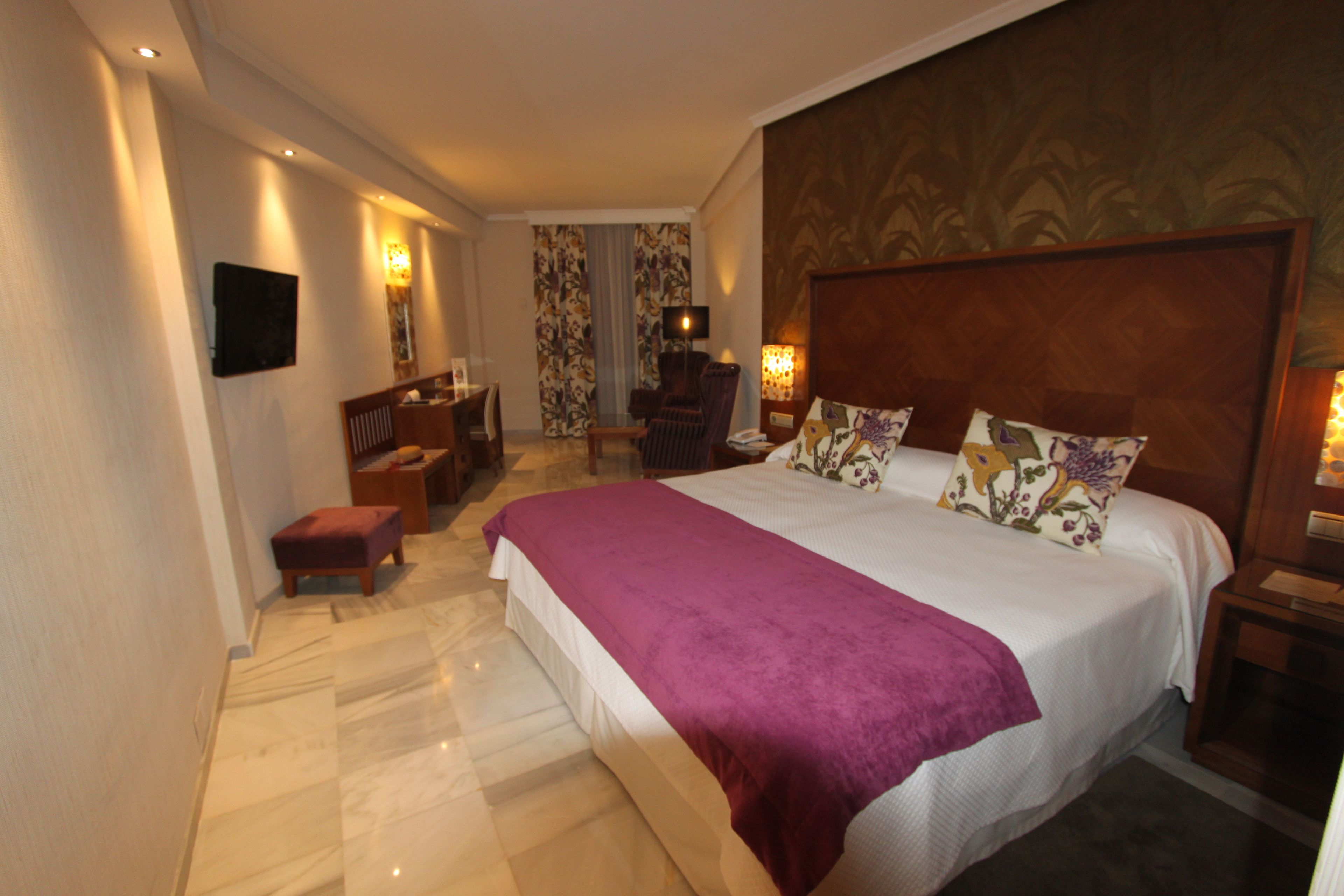 Ein Hotelzimmer mit einem großen Bett, einem Schreibtisch, einem Sessel und einem an der Wand montierten Fernseher.