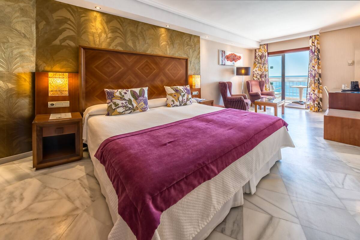 Een hotelkamer met een groot bed, een bureau, een stoel en een balkon met uitzicht.