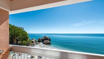 A balcony with a view of a beach, rocky outcrops, and clear blue sea.