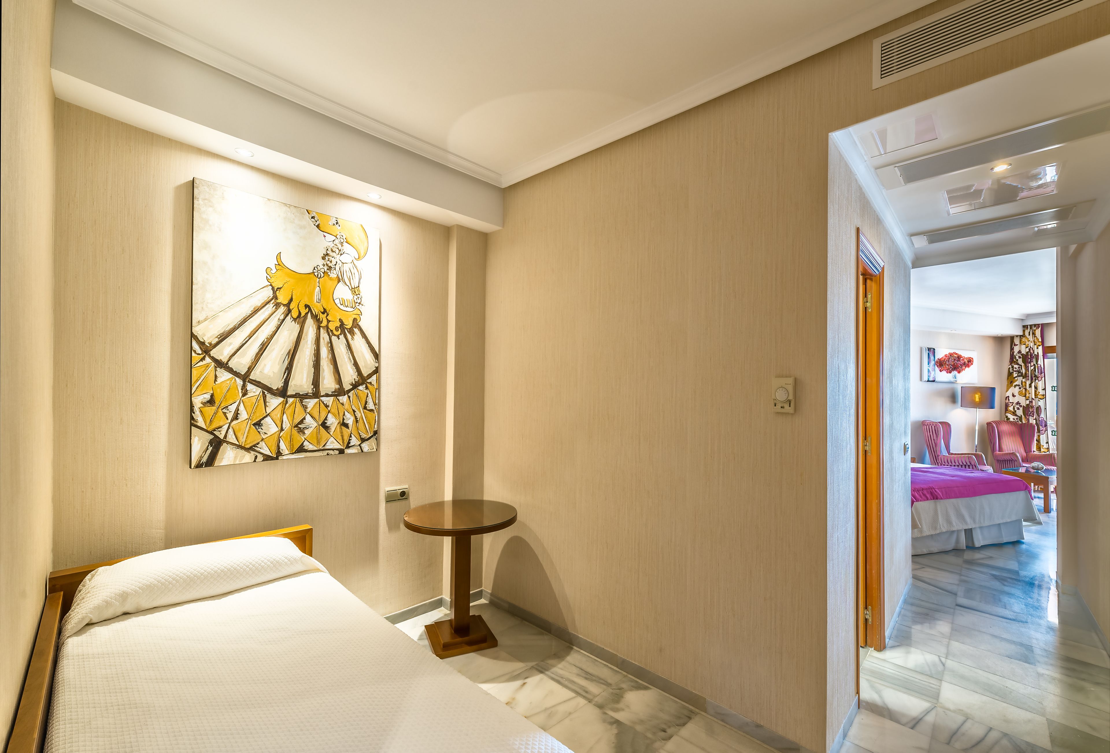 A hotel room with a bed, a small round table, and a painting on the wall.
