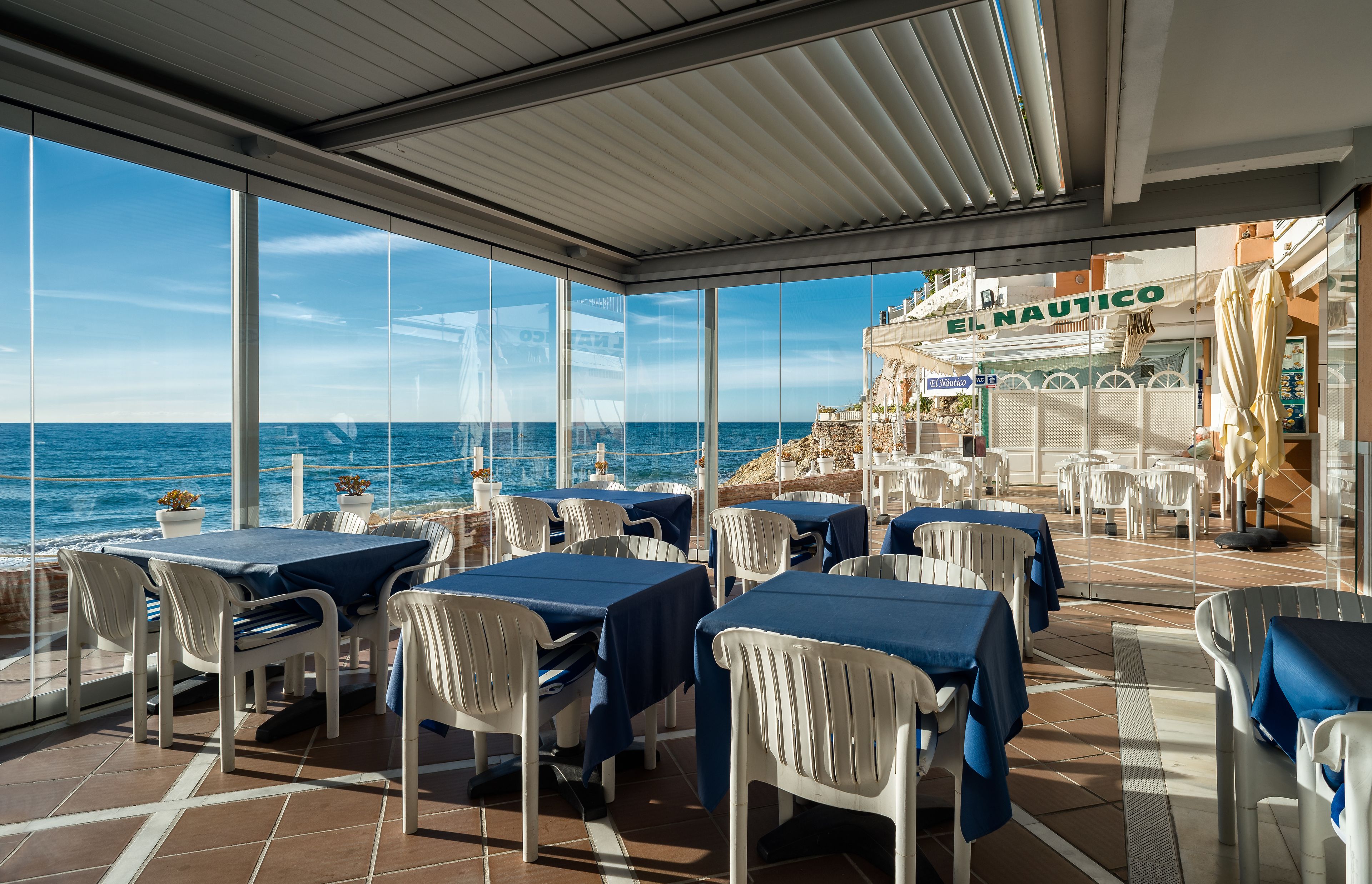 Un área de comedor al aire libre con mesas y sillas, con vista al mar.