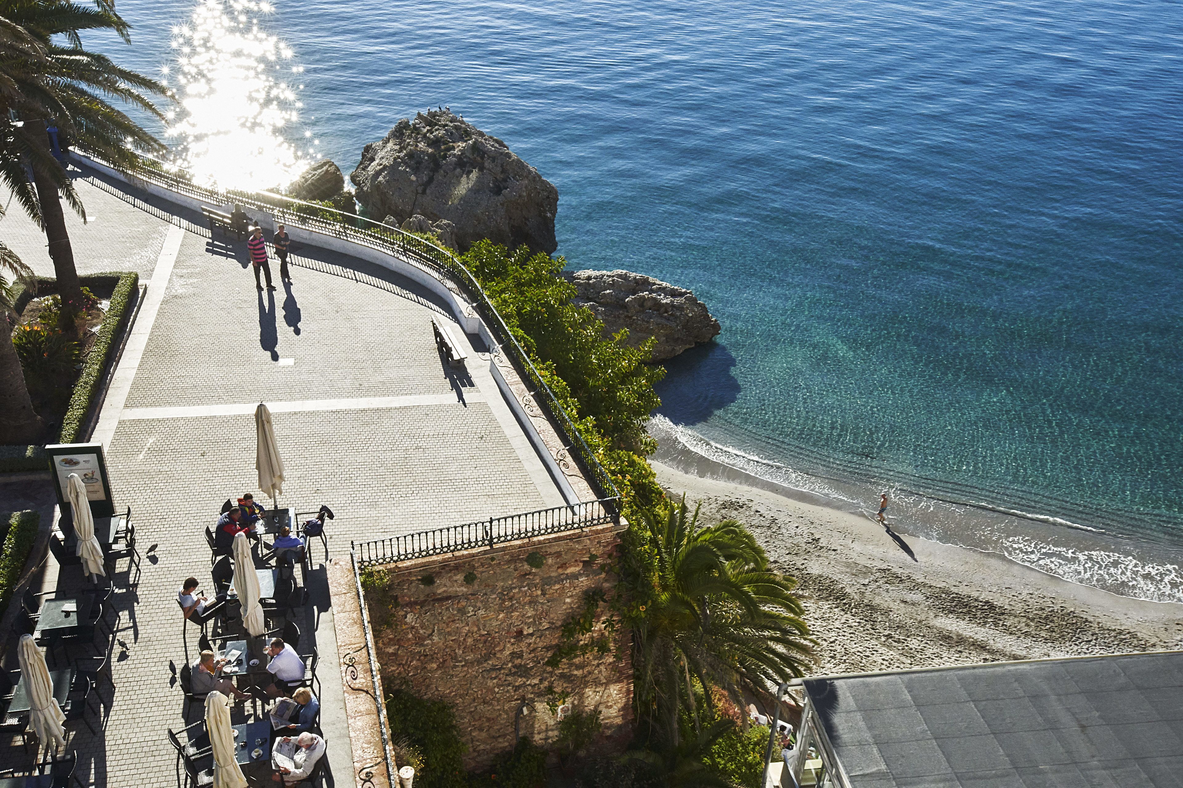 A seaside terrace with outdoor seating, overlooking the beach and ocean.