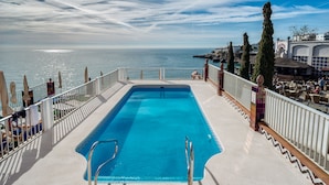 Una piscina con vista al mar, rodeada por una barandilla blanca y sombrillas.