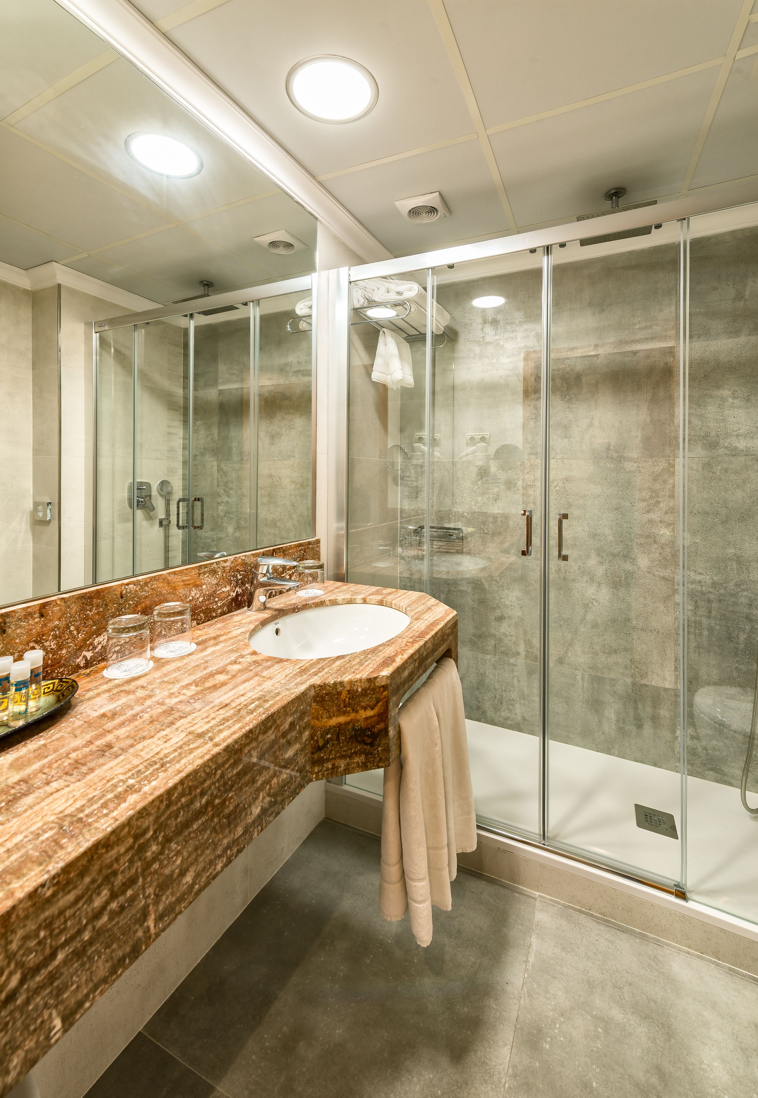 A modern bathroom with a marble countertop, a glass shower enclosure, and a large mirror.