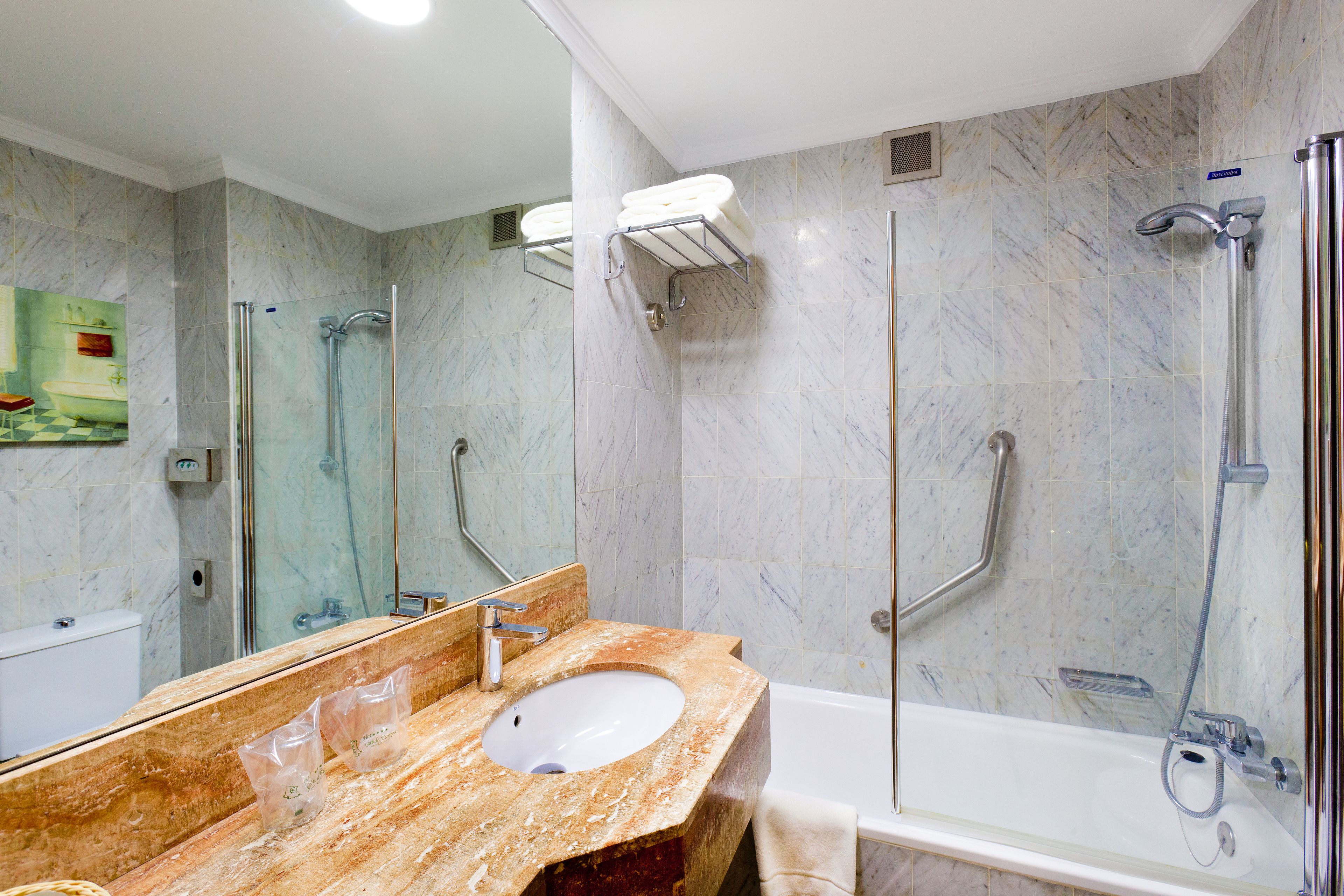 Un baño con lavamanos de mármol, bañera y ducha con cerramiento de vidrio.
