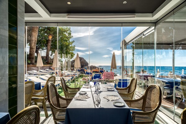 Un área de comedor al aire libre con sillas y mesas de mimbre, con vista al mar.